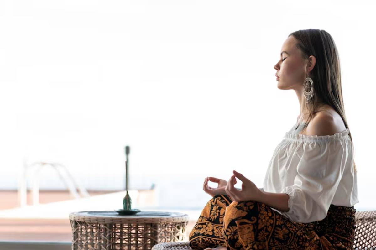 A woman in a white off-shoulder top and patterned pants meditates in a serene space, exuding calm and tranquility.