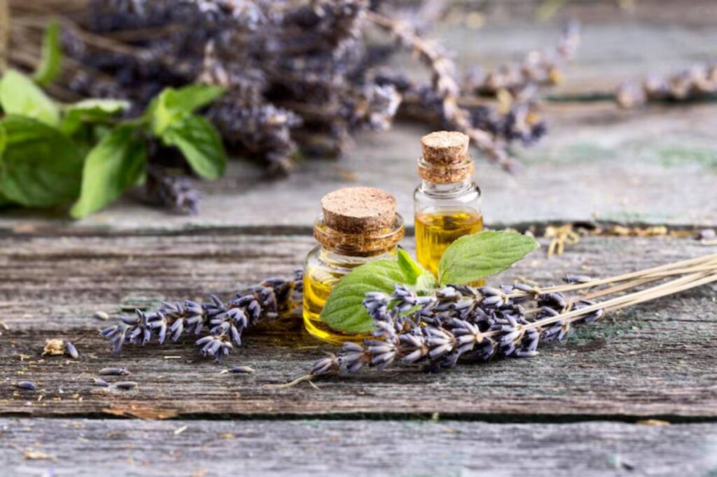 Two glass bottles of essential oil surrounded by lavender sprigs and green leaves on a rustic wooden surface.