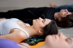 Three individuals lie on yoga mats in a relaxed position, focusing on mindfulness and tranquility during a class.