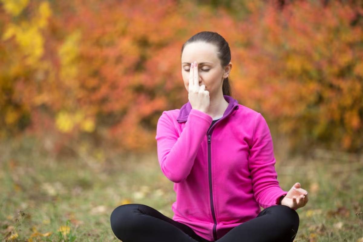 A person in a pink jacket practices mindfulness in a serene outdoor setting, surrounded by vibrant autumn foliage.