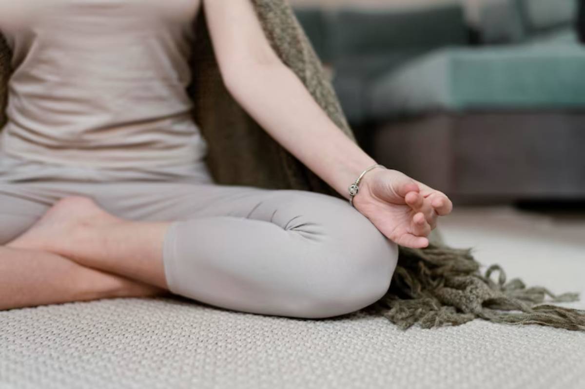 A person sits cross-legged in a serene environment, practicing meditation with a calm posture and hand signal for mindfulness.