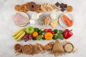 An assortment of healthy foods including fruits, vegetables, proteins, grains, and snacks beautifully arranged on a light background.