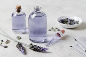 Two glass bottles filled with lavender oil, a dropper, and dried lavender flowers on a light surface.