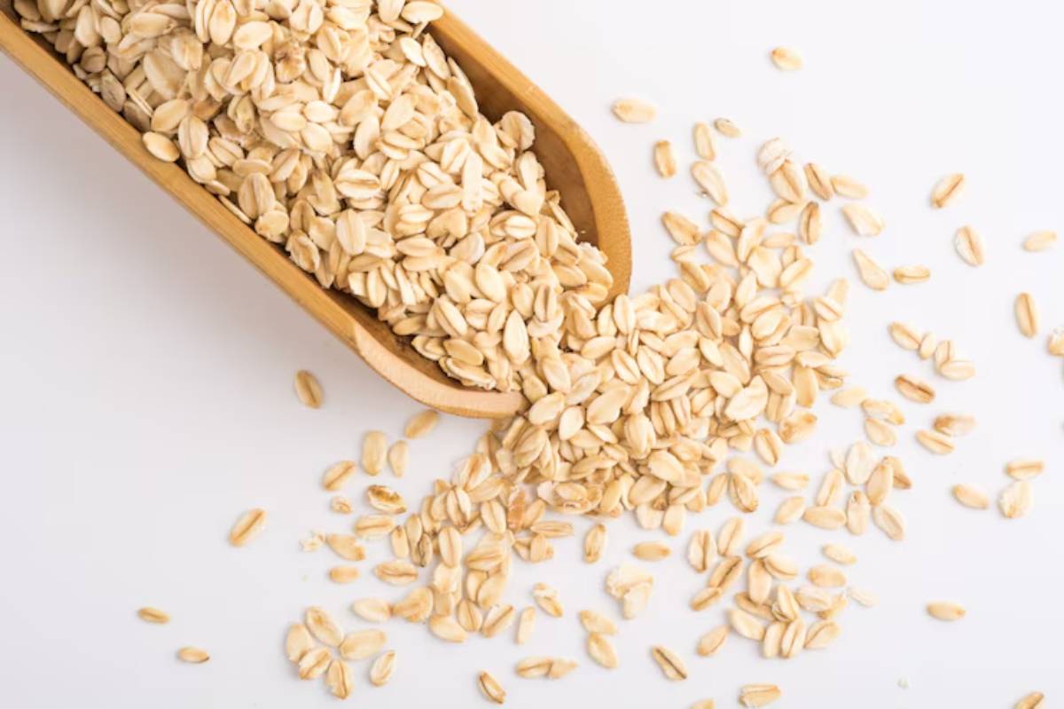 A wooden scoop overflowing with rolled oats, some spilling onto a clean white surface.