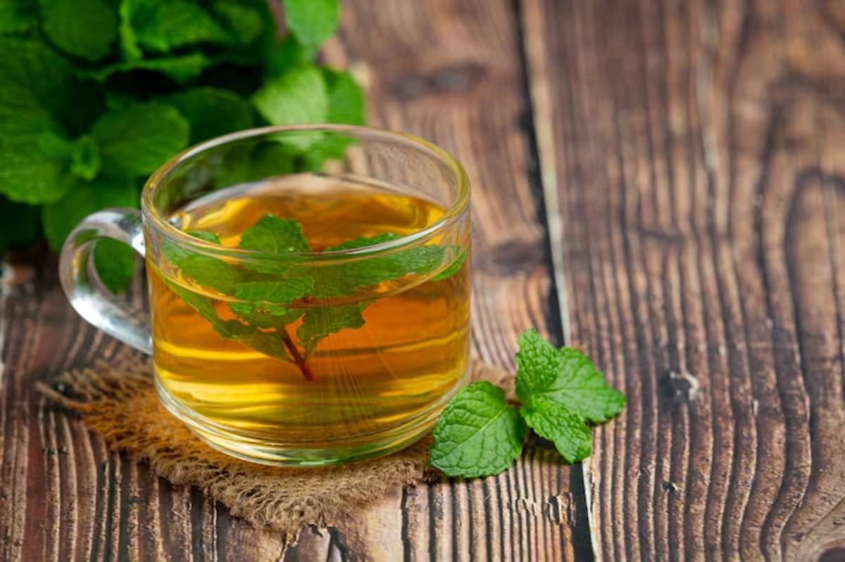 A glass cup filled with herbal tea, garnished with fresh mint leaves, placed on a rustic wooden table.