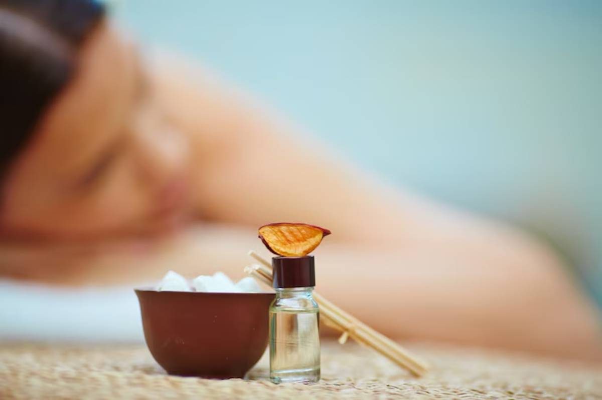 A relaxing spa scene featuring a bottle of essential oil, a bowl of ice, and a blurred background of a person receiving a massage.