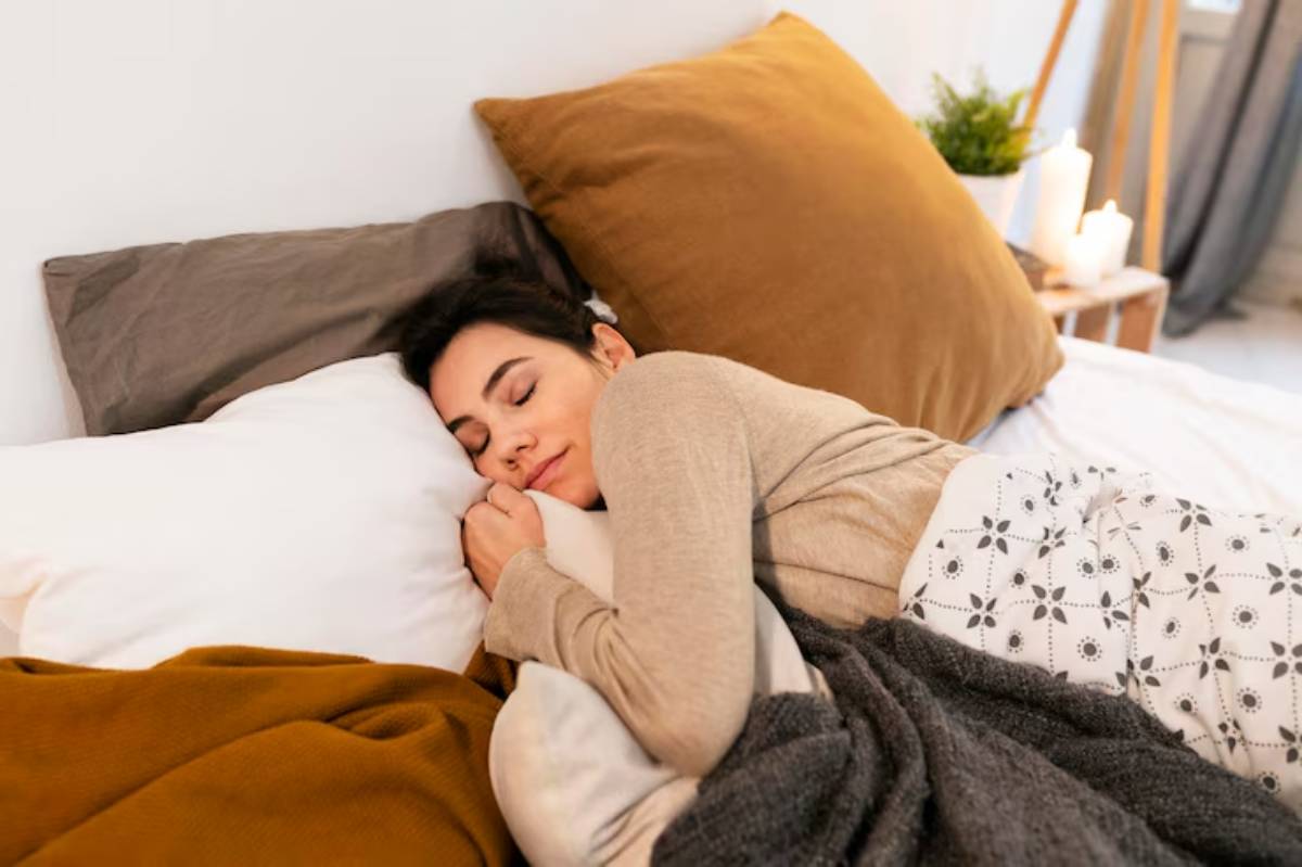 A person cuddles a pillow on a cozy bed adorned with warm blankets and decorative pillows in a serene, softly lit room.