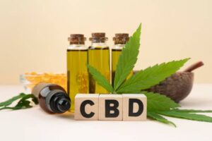Bottles of CBD oil, a dropper bottle, a cannabis leaf, and wooden blocks spelling "CBD" arranged artistically on a soft background.