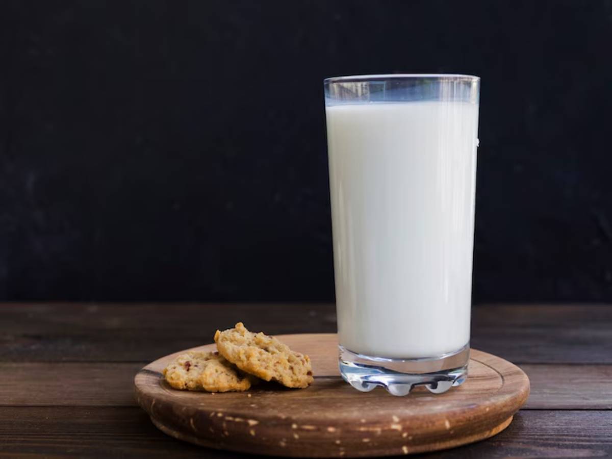 A tall glass of milk beside two cookies on a wooden platter, against a dark background, creating a cozy snack scene.