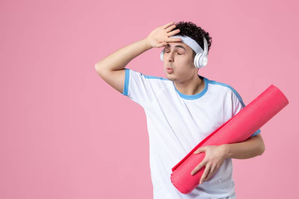 A young person wearing headphones holds a pink yoga mat, striking a playful pose against a pastel pink background.