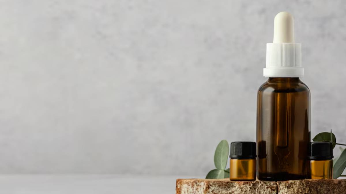 A wooden slice holds a dark glass dropper bottle and two smaller oil bottles, with green leaves nearby against a light grey background.