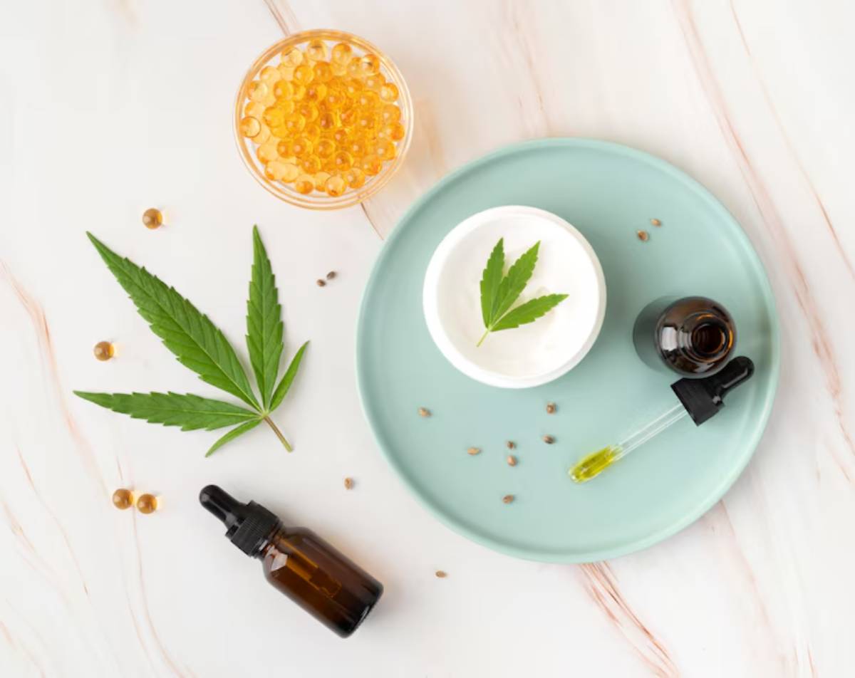 A flat lay of cannabis products, including a cream with a leaf, oil dropper, amber bottle, and yellow capsules on a green plate.