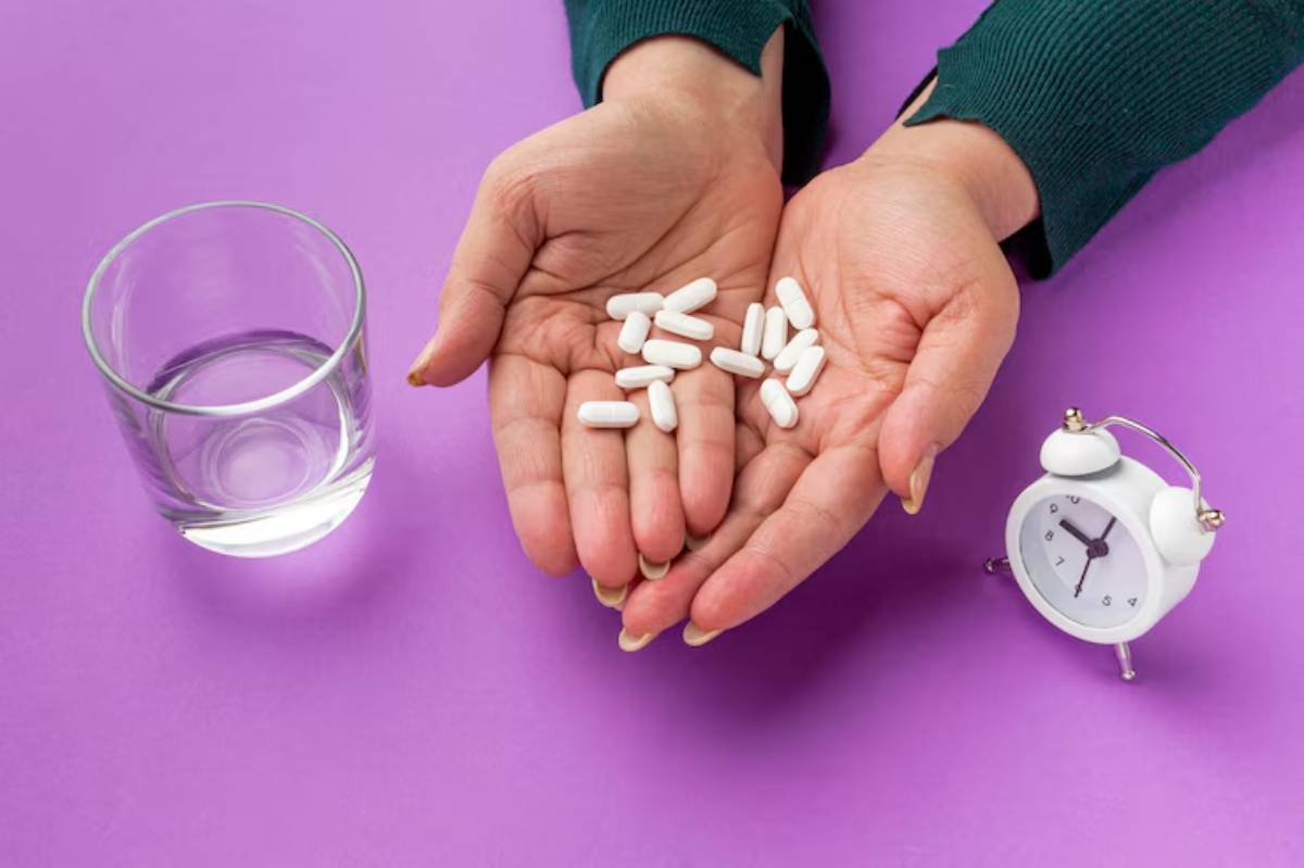 Two hands hold white pills above a glass of water and a small alarm clock on a purple background. 