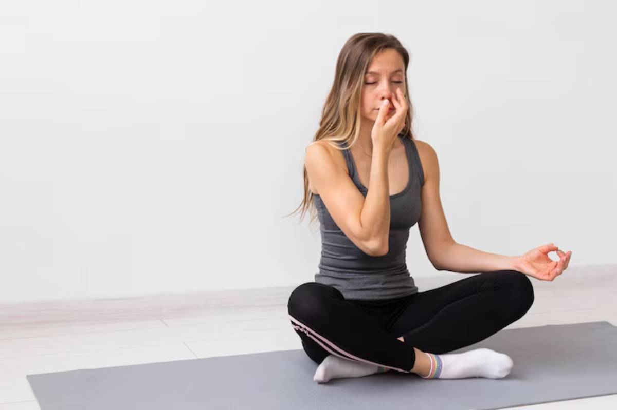 A woman sits cross-legged on a yoga mat, practicing meditation and breathing techniques in a serene indoor setting.