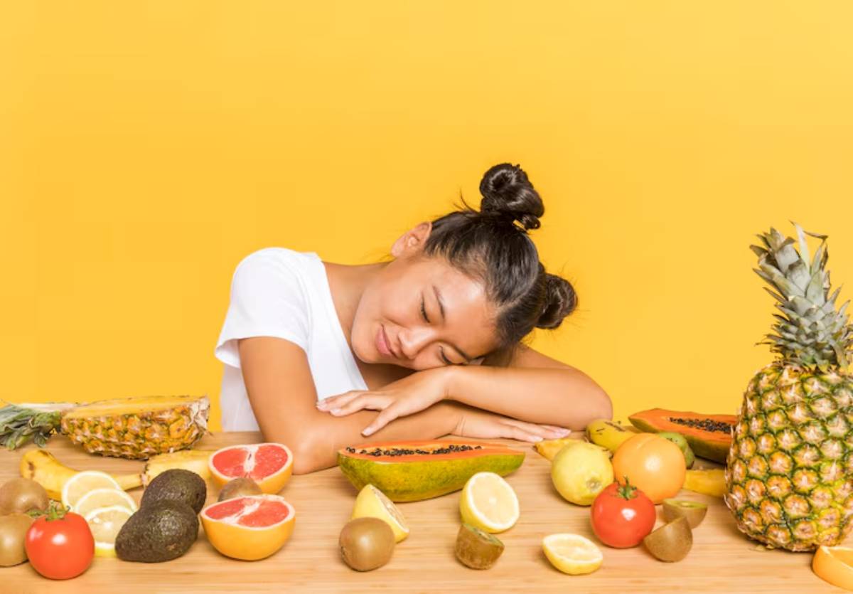 A variety of colorful fruits including pineapple, papaya, and citrus are scattered on a wooden table against a bright yellow background.